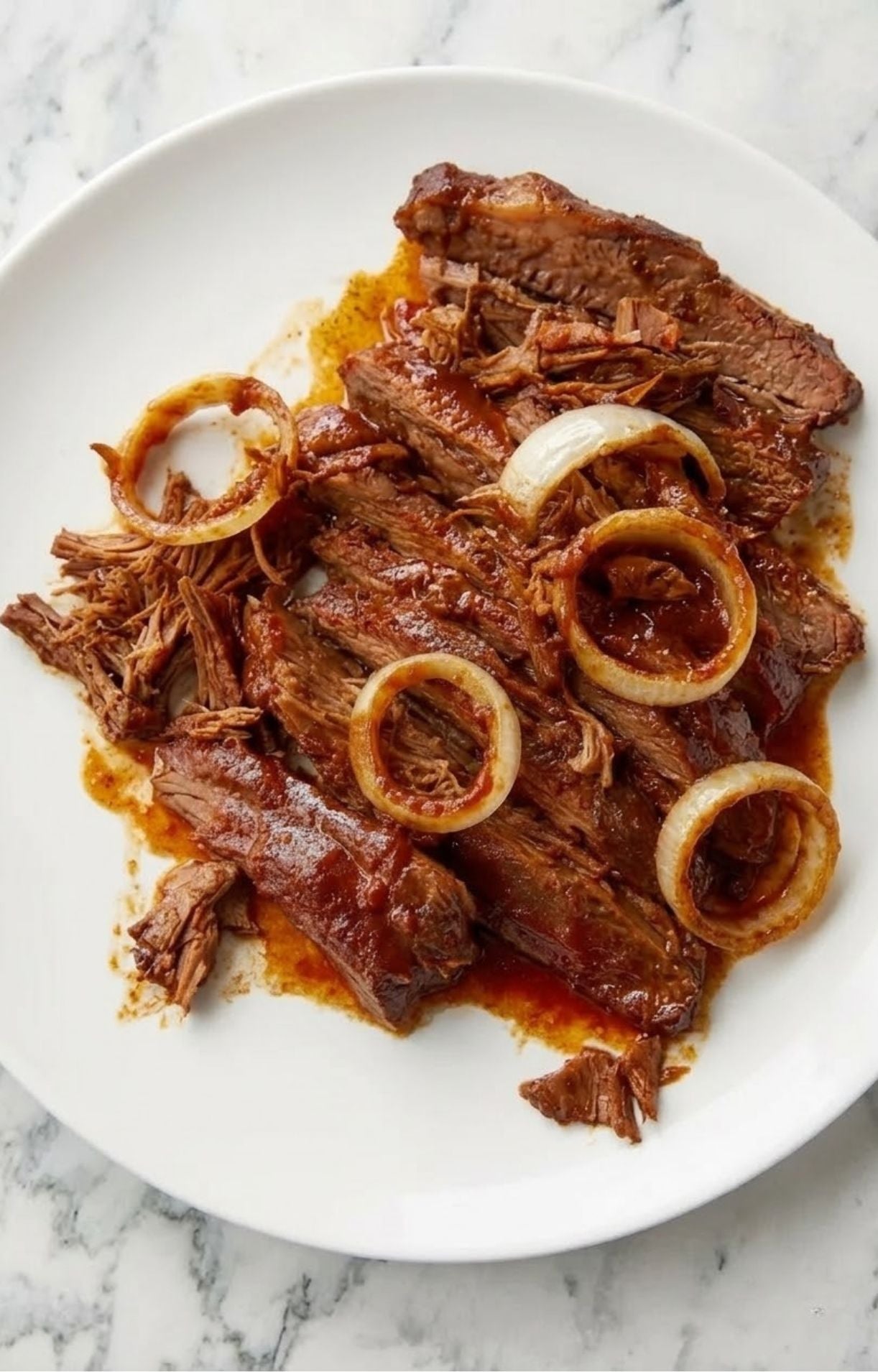 Slices of juicy beef brisket served on a white plate with tender cooked onion rings and savory au jus.