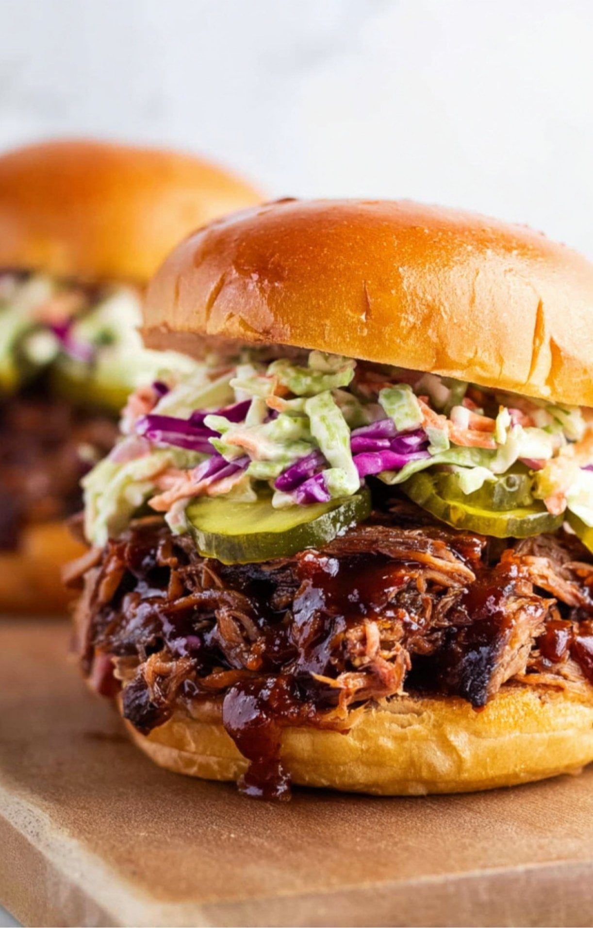A side profile of a brisket sandwich highlighting the thick-cut pickles and the glossy, toasted bun.
