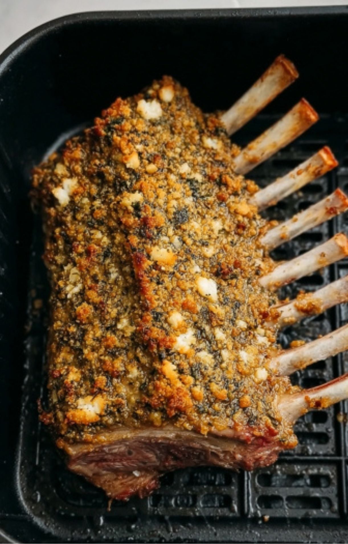 The rack of lamb inside the air fryer after cooking, featuring a deeply browned and crispy herb crust.