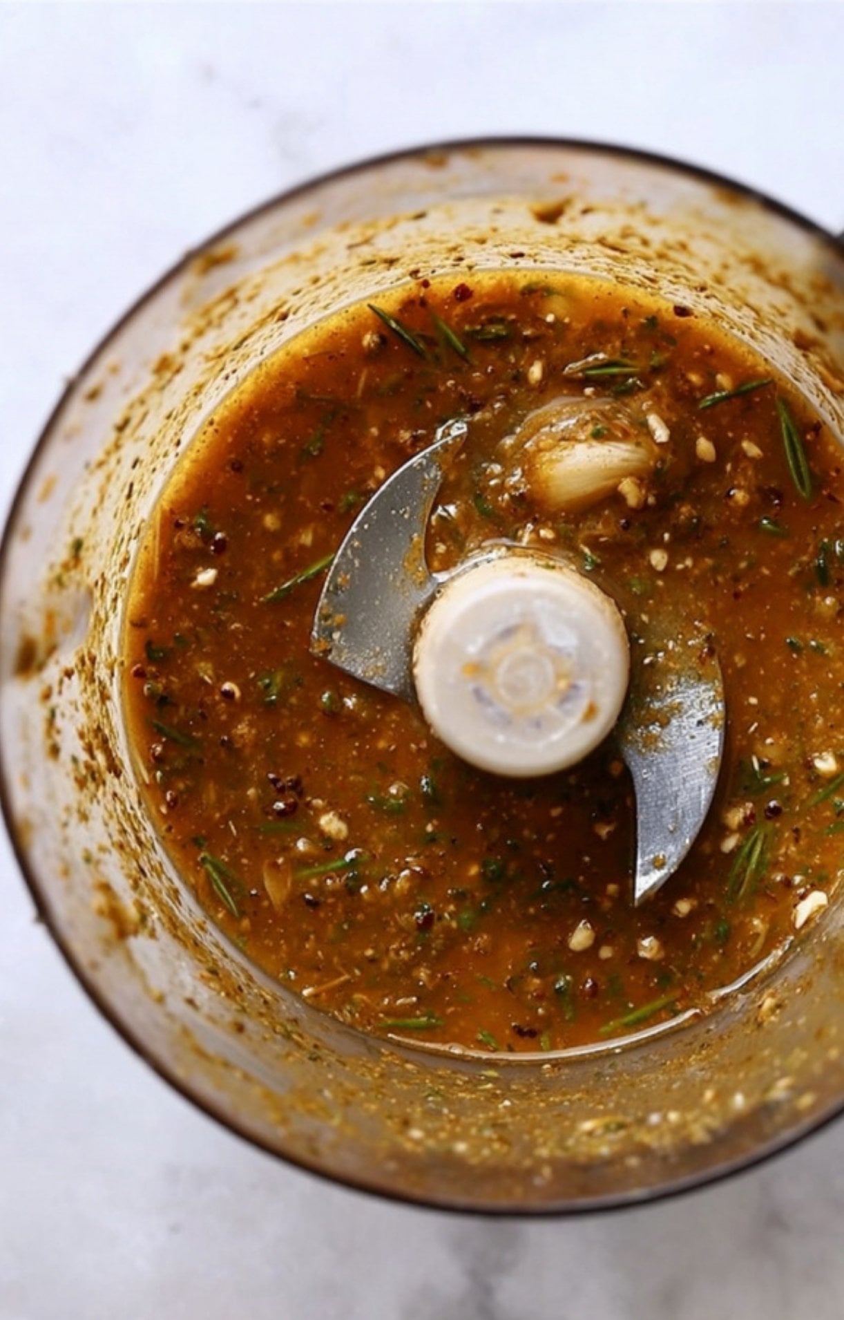 A food processor containing a blended marinade of fresh rosemary, garlic, olive oil, and spices for an air fryer lamb recipe.