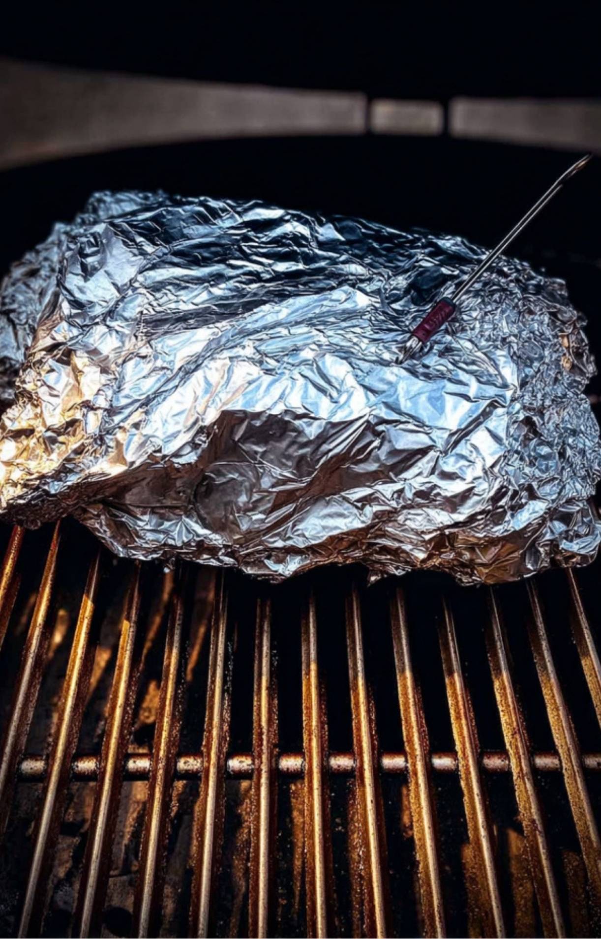 A beef brisket wrapped tightly in aluminum foil with a thermometer probe on the grill to finish an Electric Smoker Beef Brisket.
