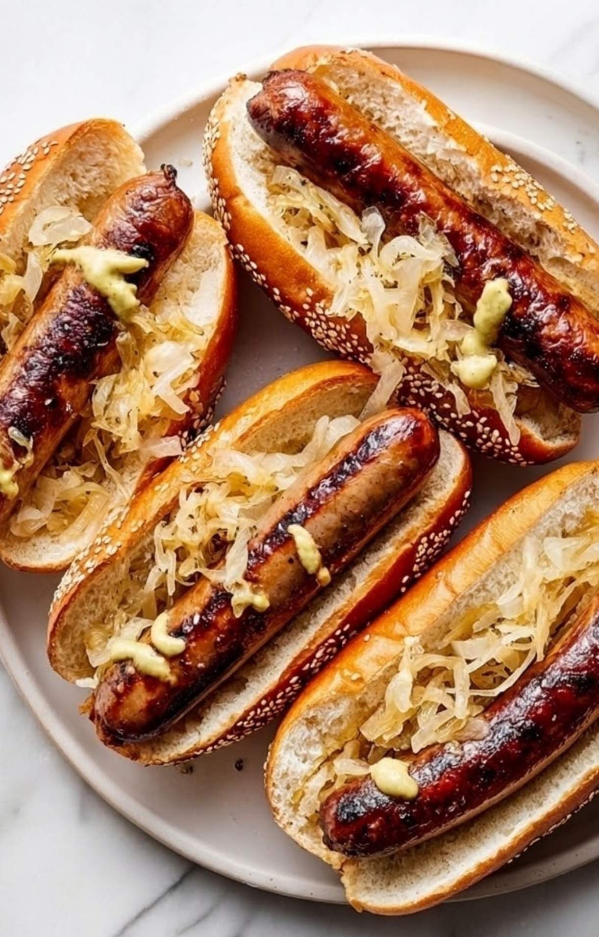 Four beer brats on grill served in buns with sauerkraut and mustard arranged on a white serving plate.