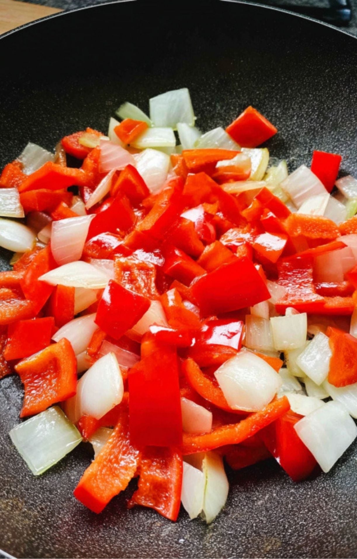 Chunks of white onion and red bell pepper being stir-fried in a black wok until slightly softened.