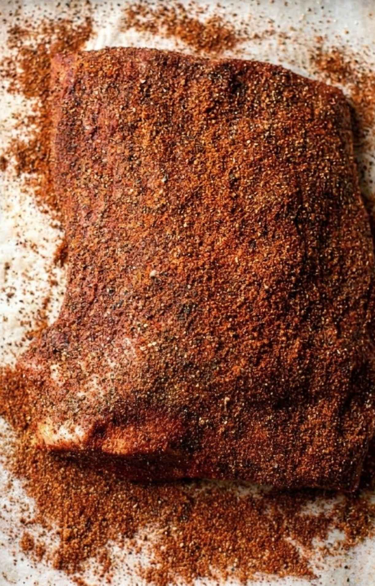 Top-down view of a beef brisket heavily coated in a dark, textured dry rub seasoning.