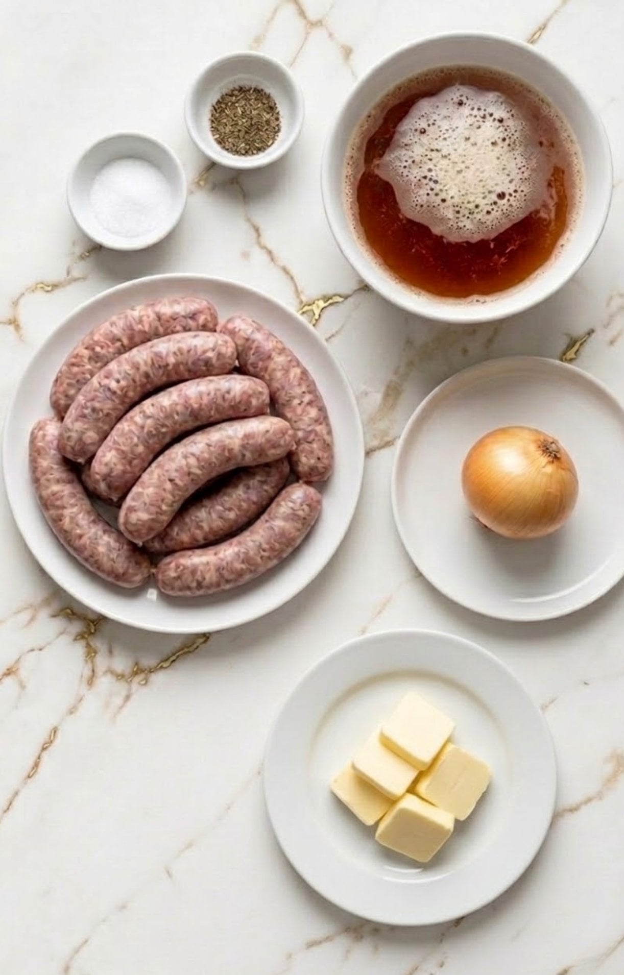 Raw bratwurst sausages, a whole onion, butter pats, a bowl of beer, and spices on a marble surface.