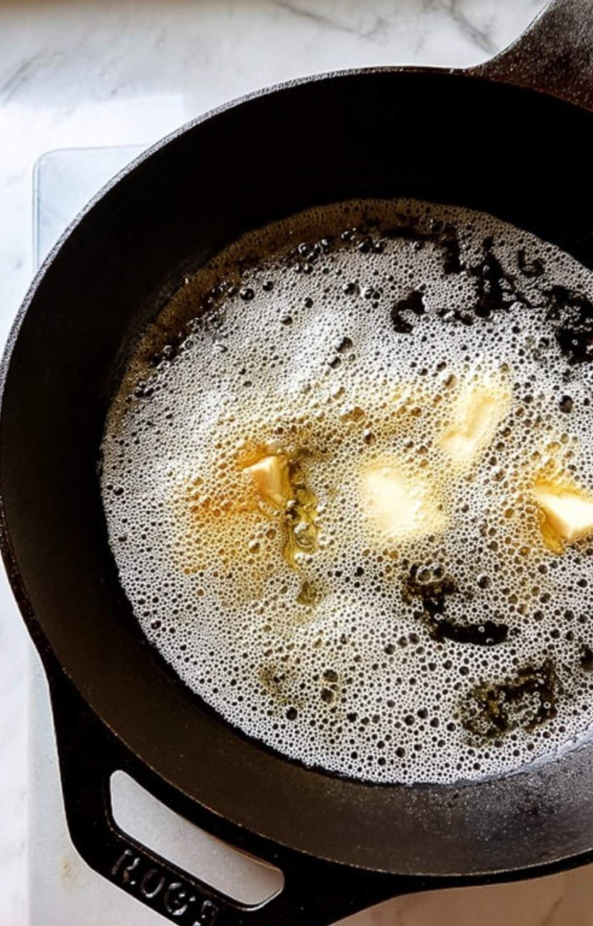 Butter melting and foaming in a hot cast iron skillet to prepare for searing beer brats.