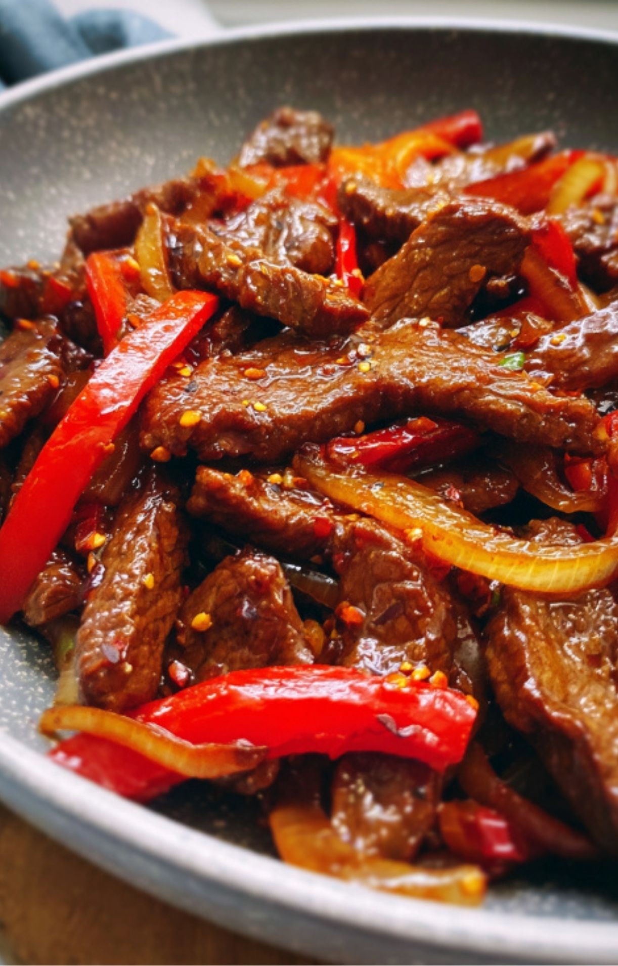 A close-up view of the completed Beijing Beef stir-fry still in the pan, highlighting the contrast between the dark meat and bright red peppers.