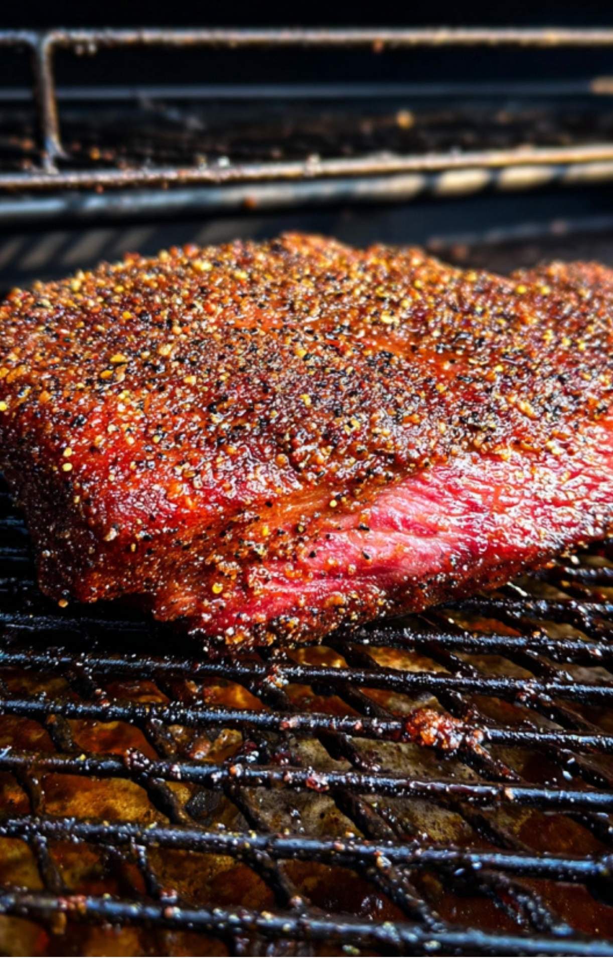 A seasoned beef brisket smoking on the black metal grates of a Traeger pellet grill.