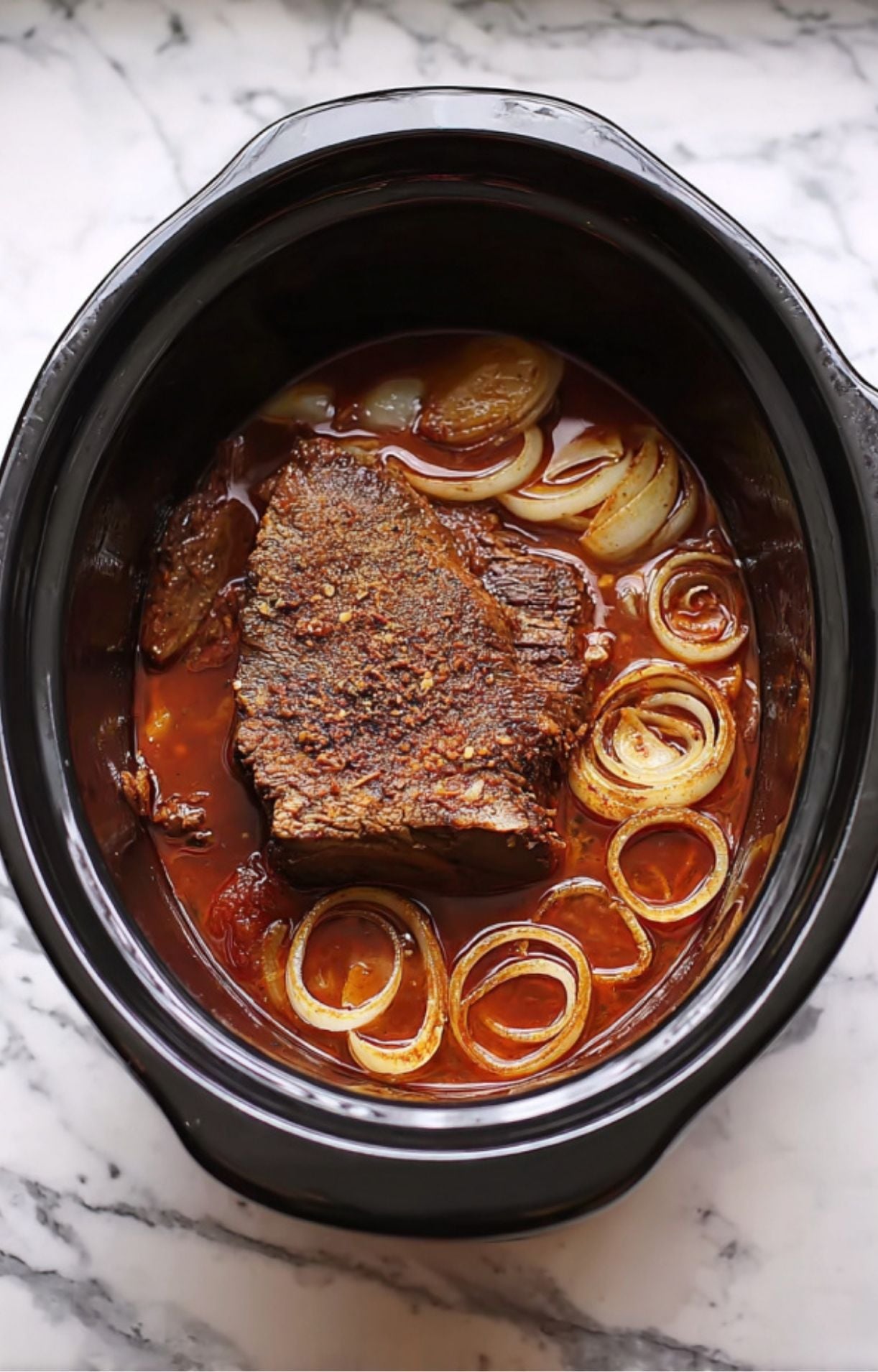 A fully cooked, tender brisket resting in a dark, flavorful braising liquid with softened onions.