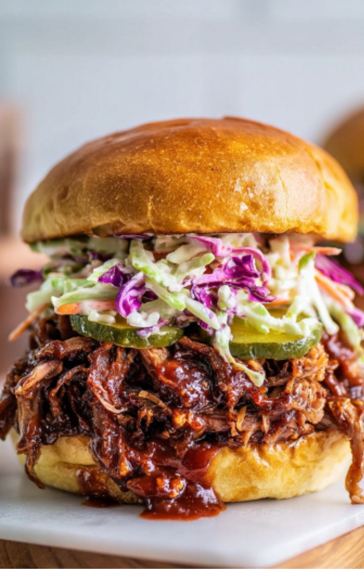 A macro shot of a finished sandwich where the barbecue sauce is dripping down the side of the shredded smoked brisket.