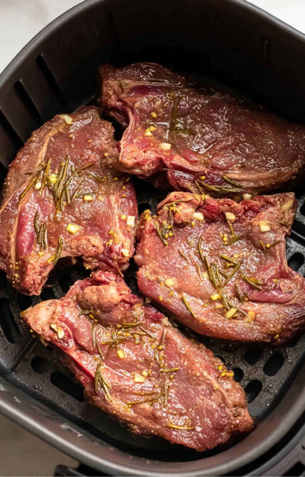 Four marinated lamb shoulder chops arranged in a single layer inside a black air fryer basket.