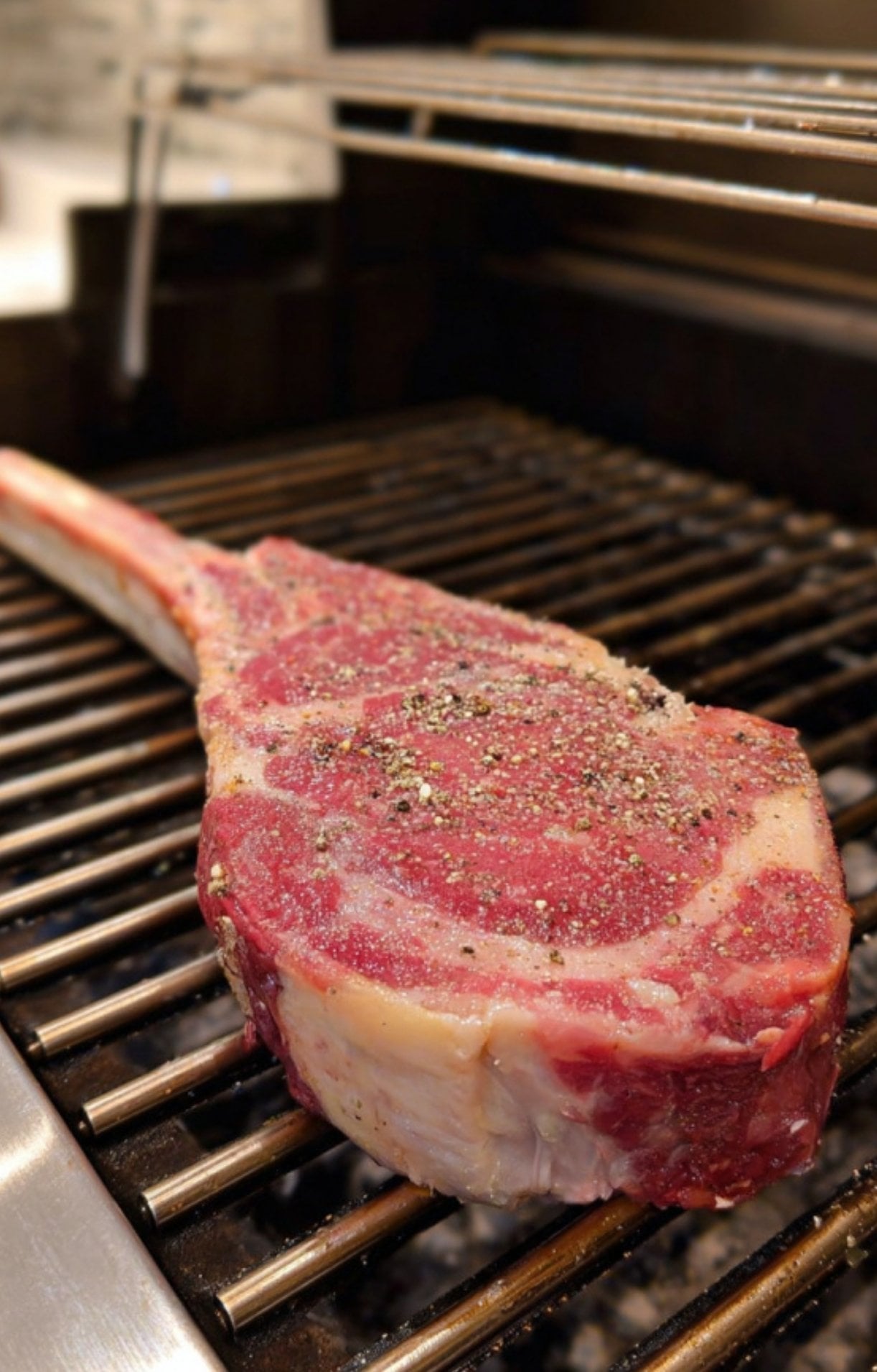 A seasoned raw tomahawk steak placed on the grill grates ready for the smoking process.