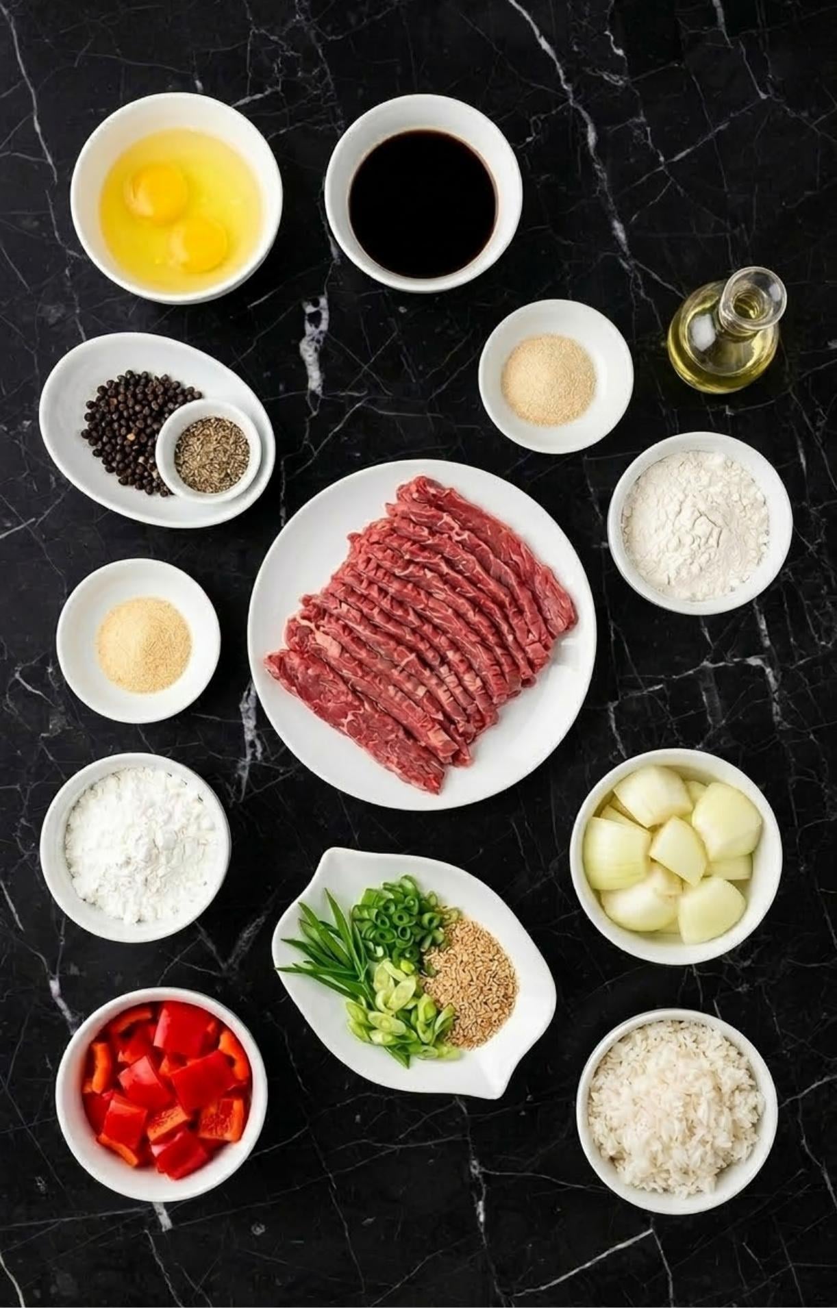 An overhead view of various ingredients including sliced flank steak, eggs, soy sauce, cornstarch, peppers, and onions on a black marble surface.