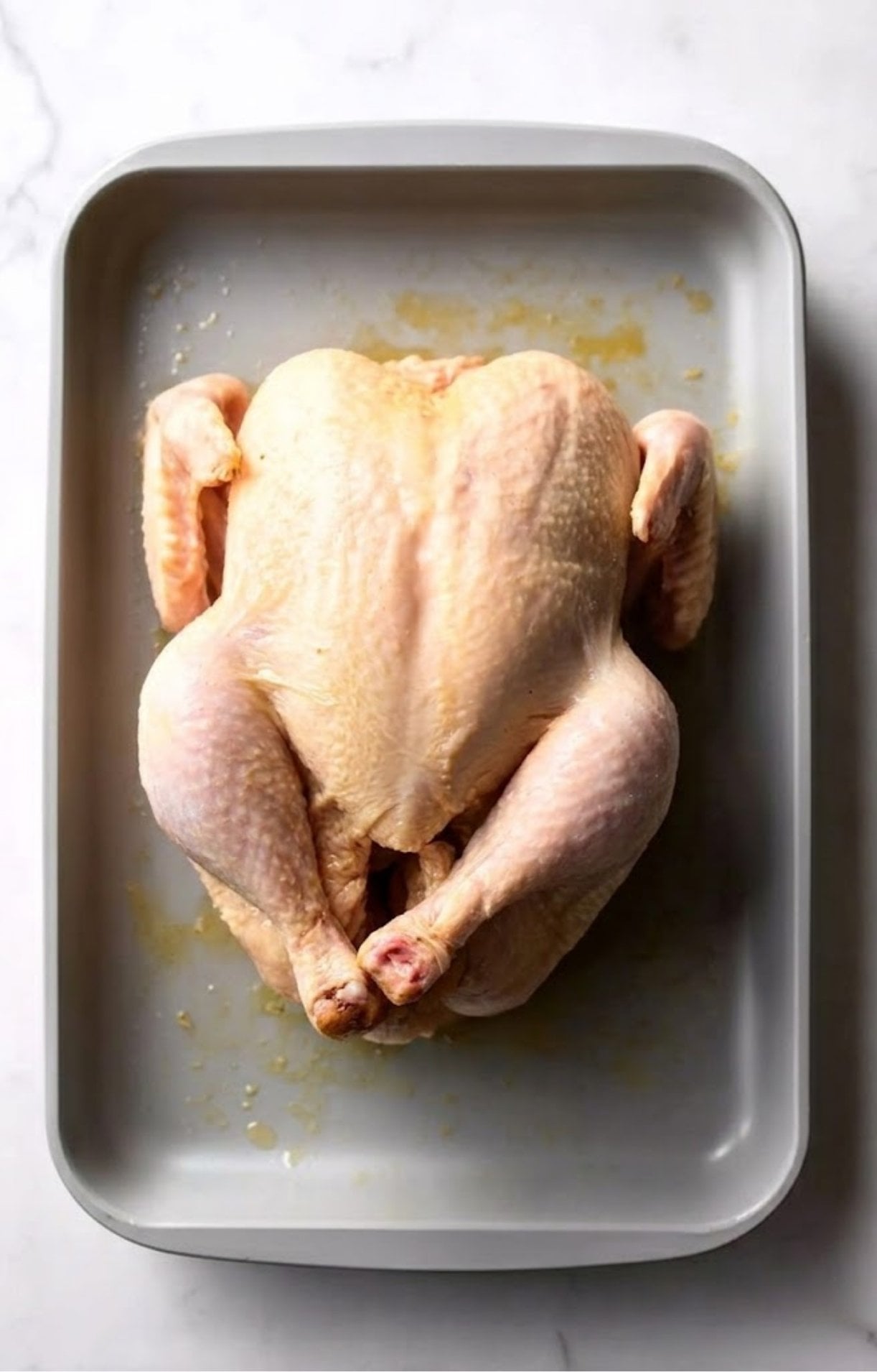 A raw whole chicken placed in a grey roasting pan, lightly coated with oil and ready for seasoning.