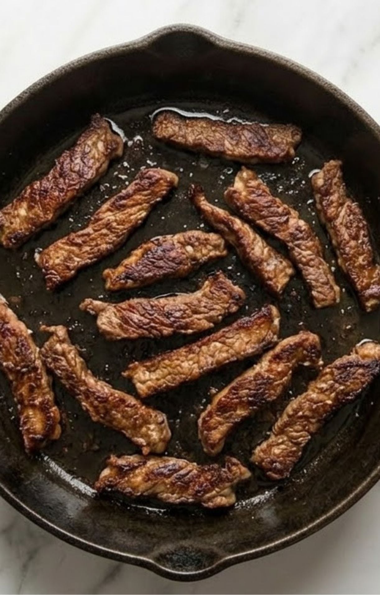 Several strips of beef being pan-seared in a dark cast-iron skillet until browned and slightly crispy on the edges for maximum flavor.