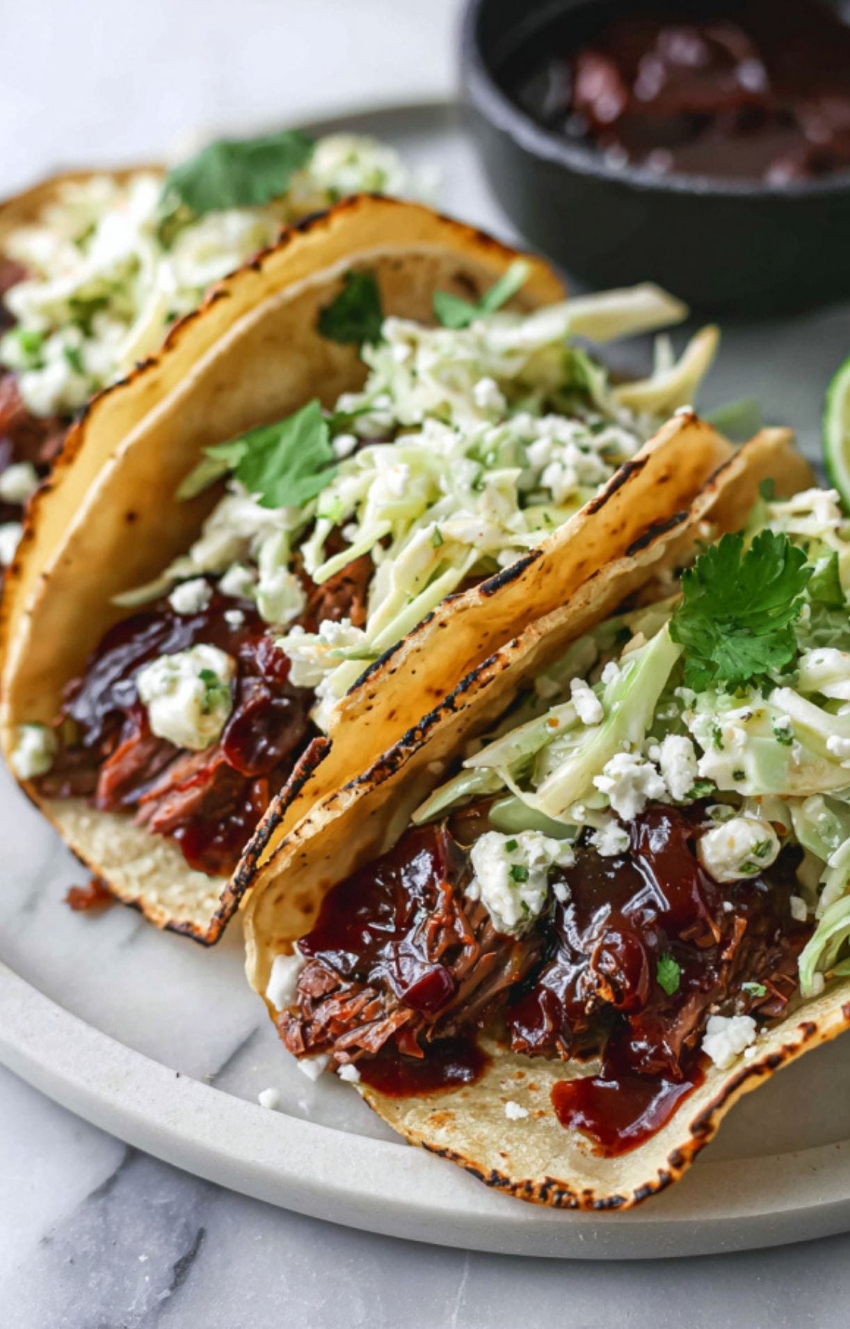 Close-up of tacos being finished with a drizzle of barbecue sauce, crumbled cheese, and fresh greens.