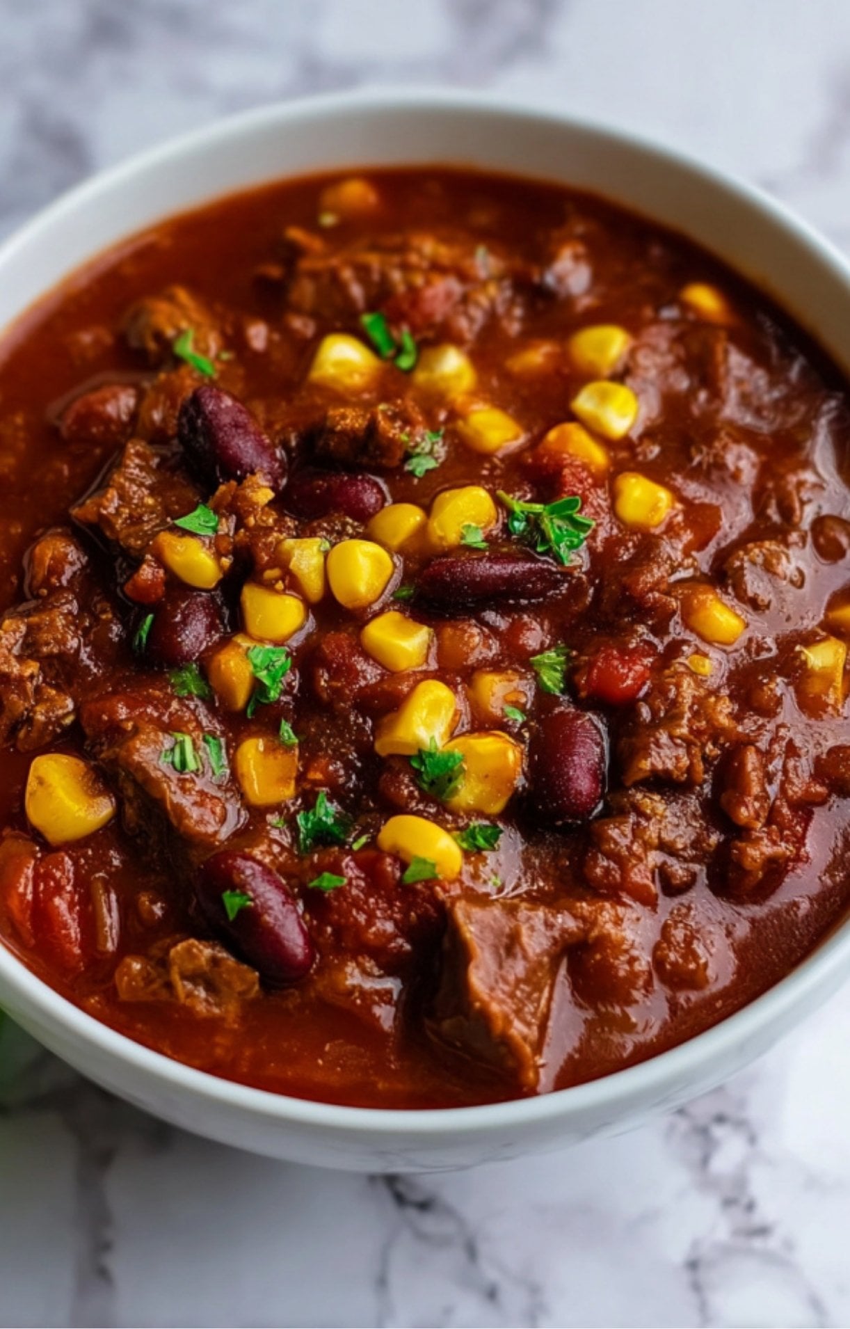 A bowl of Smoked Brisket Chili served on a marble surface, emphasizing the vibrant colors of the corn and kidney beans against the deep red sauce.
