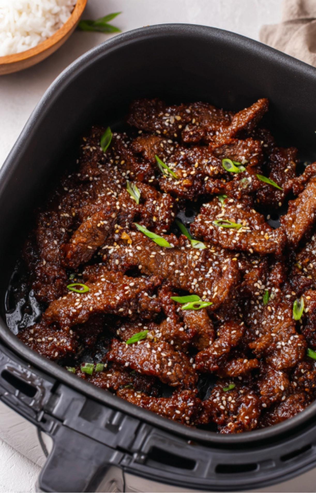 The sauced Beijing Beef back in the air fryer basket, perfectly glazed and topped with sesame seeds.