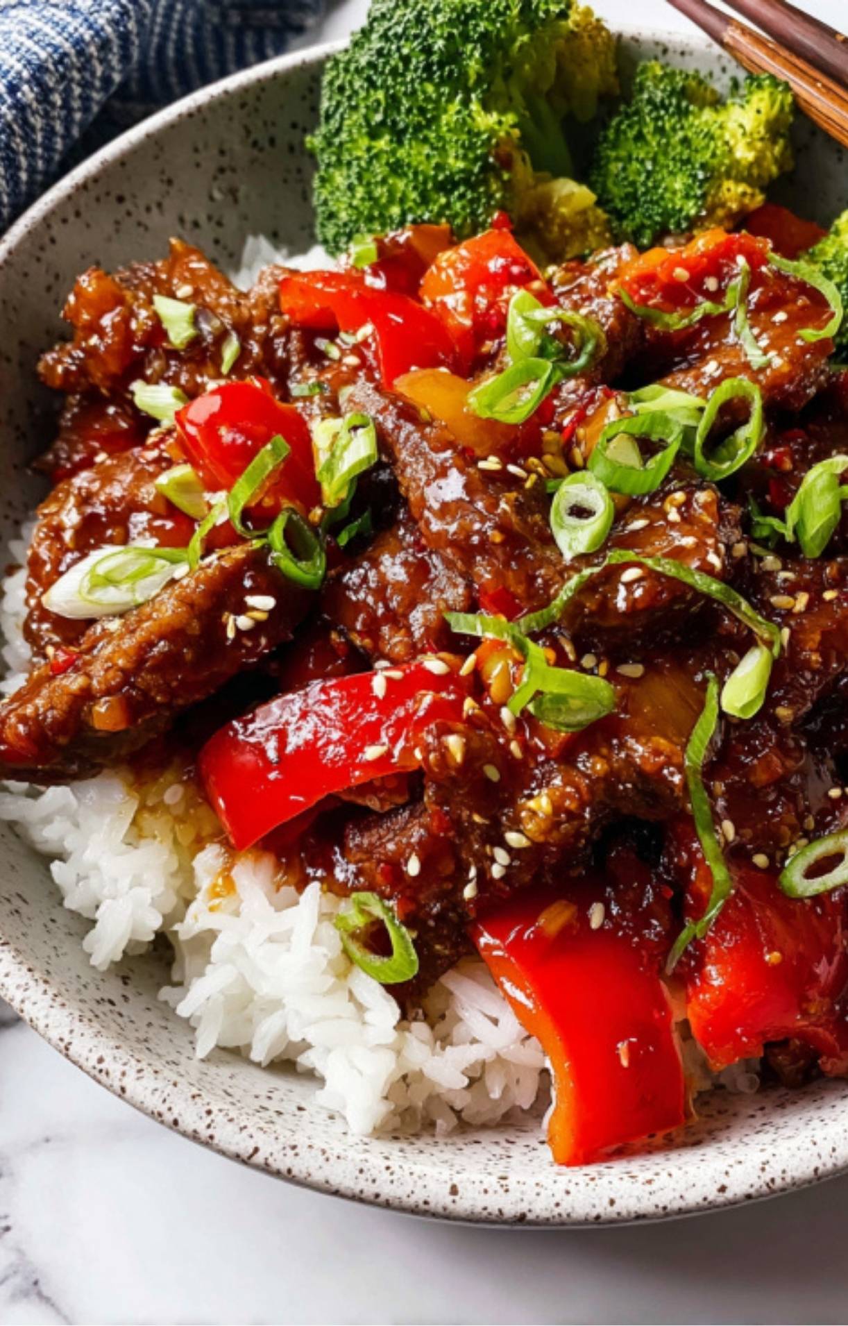 A close-up shot of Beijing Beef stir fry served over fluffy white rice, garnished with sesame seeds and fresh scallions.