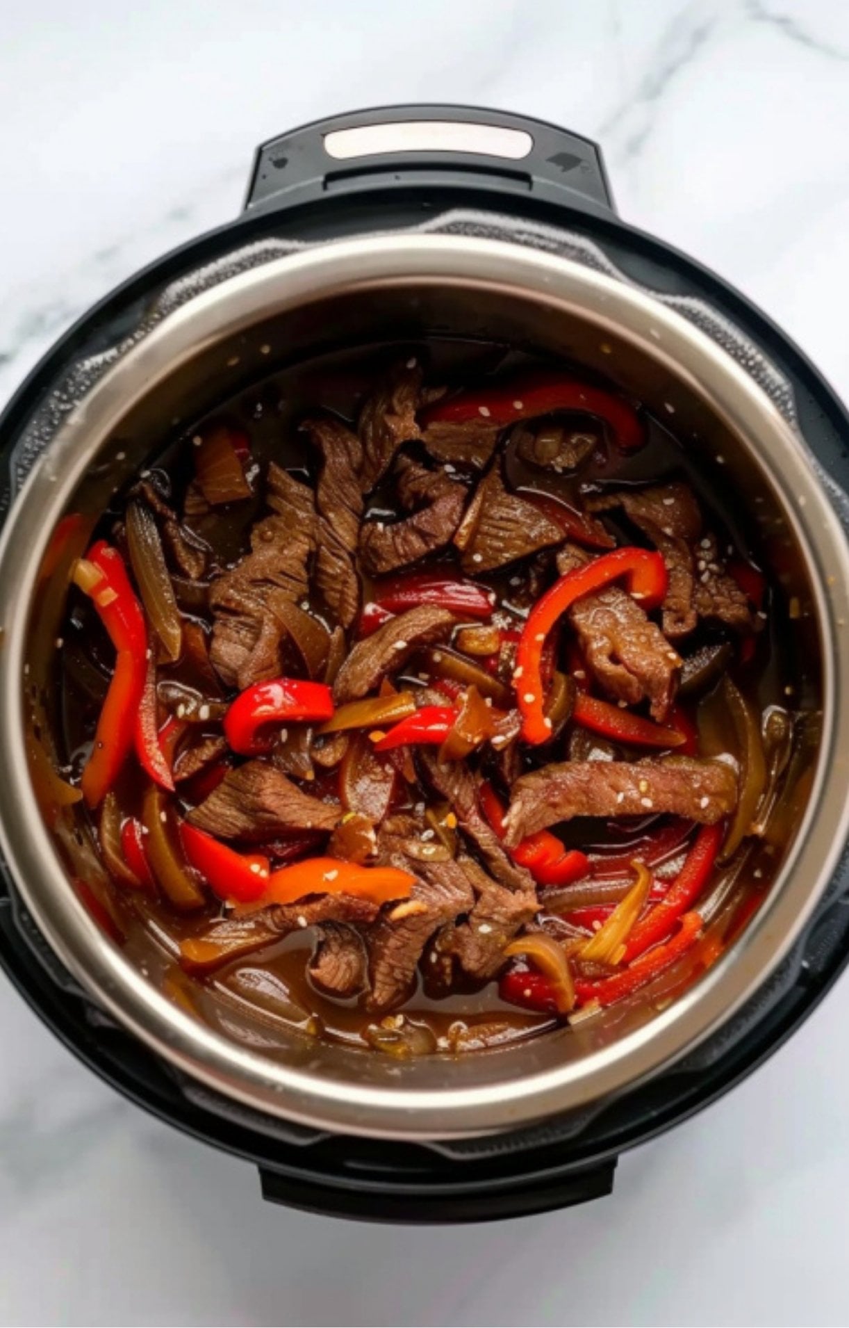 Beef strips, red bell peppers, and onions submerged in a bubbling brown sauce inside the Instant Pot during the pressure cooking or sautéing process.