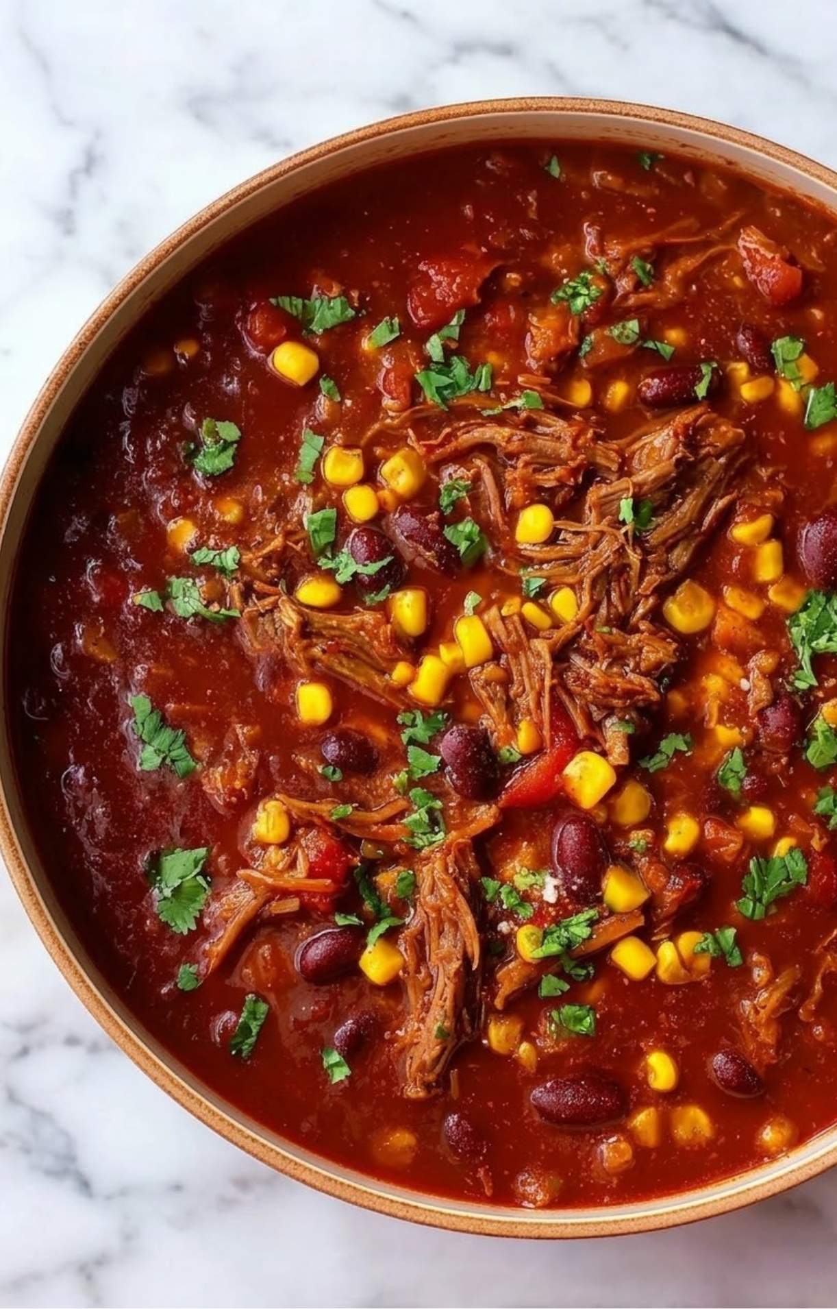 An overhead shot of a large pot of Smoked Brisket Chili topped with extra corn and a heavy sprinkle of chopped herbs.