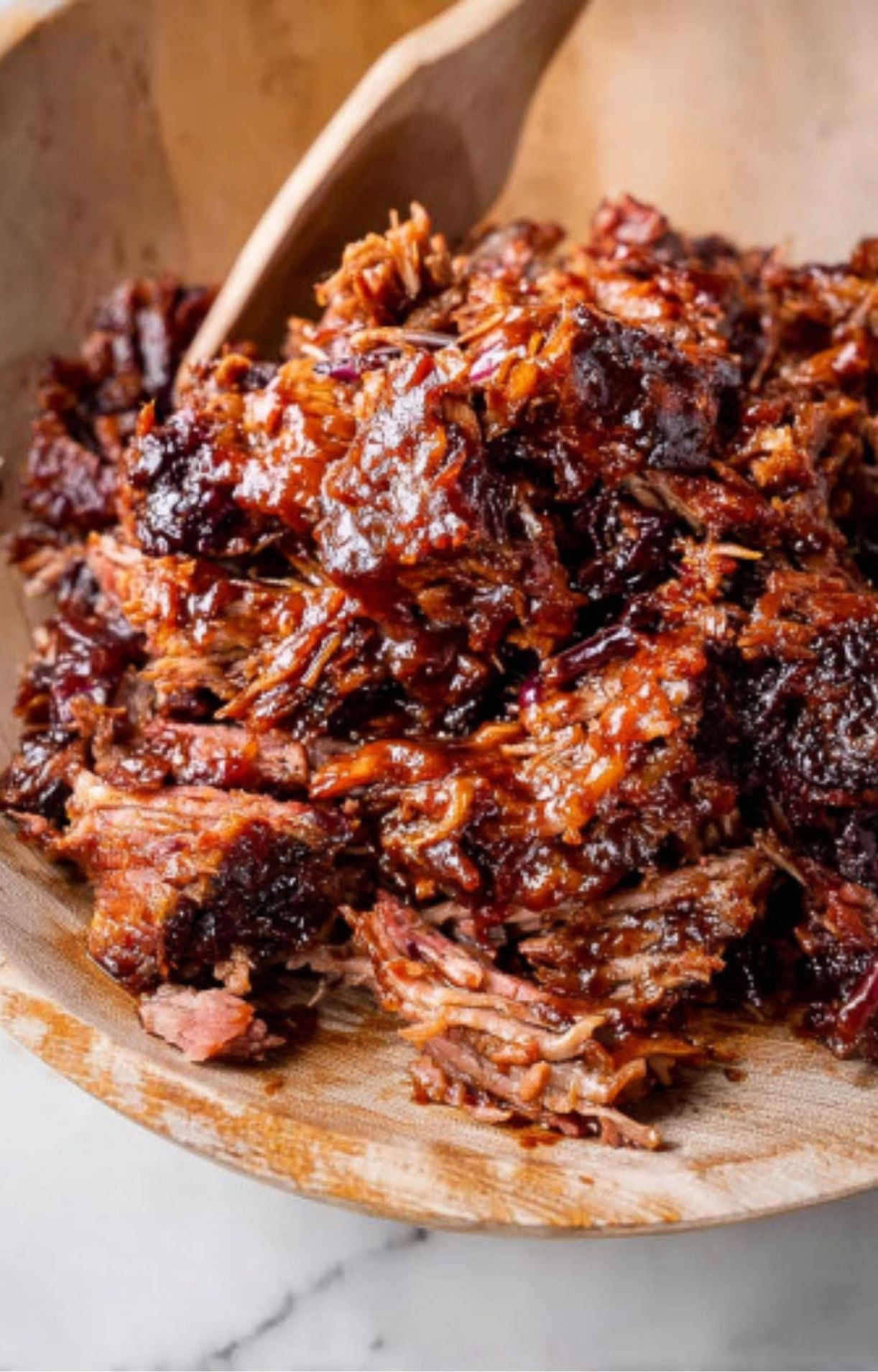 A wooden bowl filled with tender, pulled smoked brisket thoroughly coated in a rich, dark barbecue sauce.