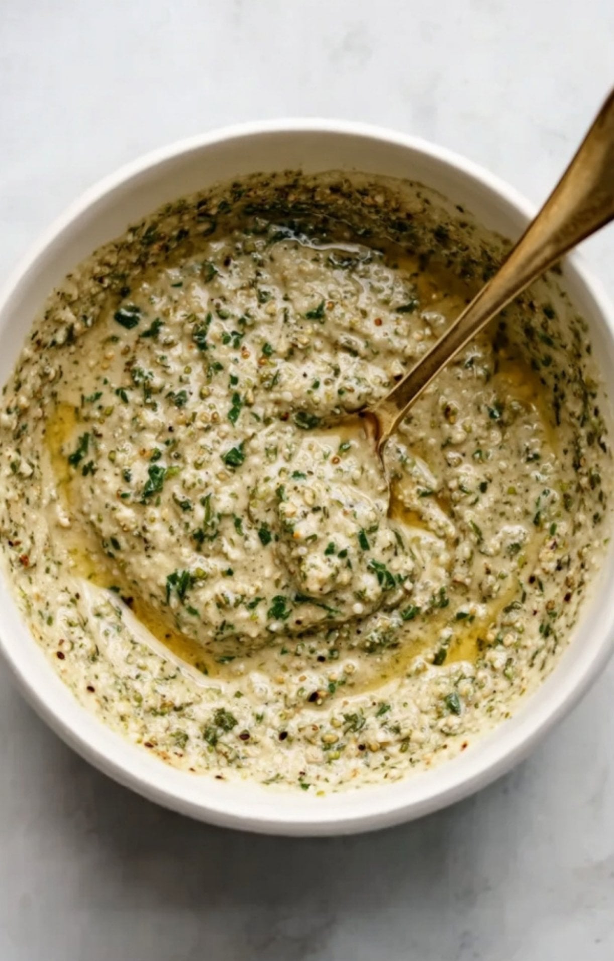 A white bowl filled with a well-blended, thick green herb and mustard paste ready to be spread on the meat.