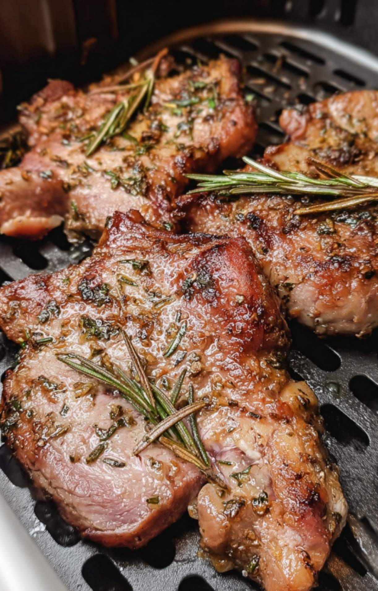 Close-up shot of thick lamb steaks cooking in an air fryer basket, featuring a golden-brown sear, fresh rosemary sprigs, and a savory herb rub.