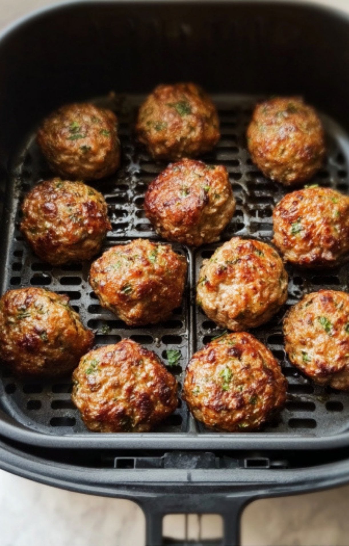 The finished meatballs inside the air fryer basket, showing a deep brown sear and rendered fat.