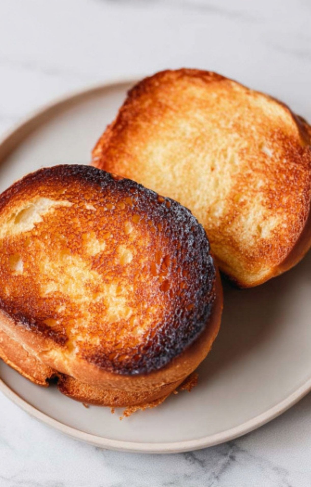 Two halves of a brioche bun toasted to a golden-brown finish on a light-colored plate.