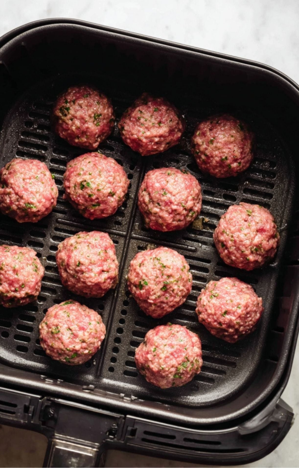 Raw lamb meatballs spaced out evenly in a black air fryer basket before the cooking process begins.