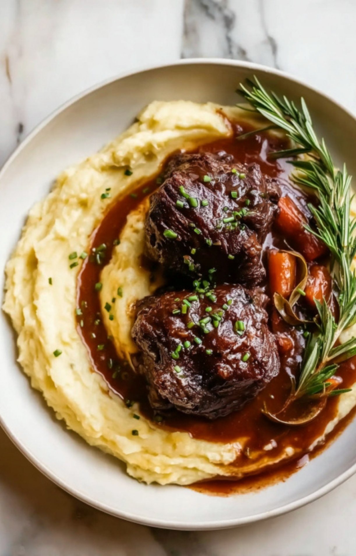 An overhead shot of succulent beef cheeks on a bed of silky mashed potatoes, drizzled with a dark red wine reduction and sprinkled with chives.