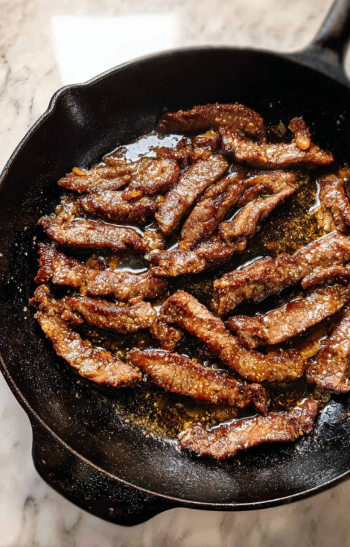 Strips of beef searing in a hot cast-iron skillet with a light glaze during the Beijing Beef stir fry cooking process.