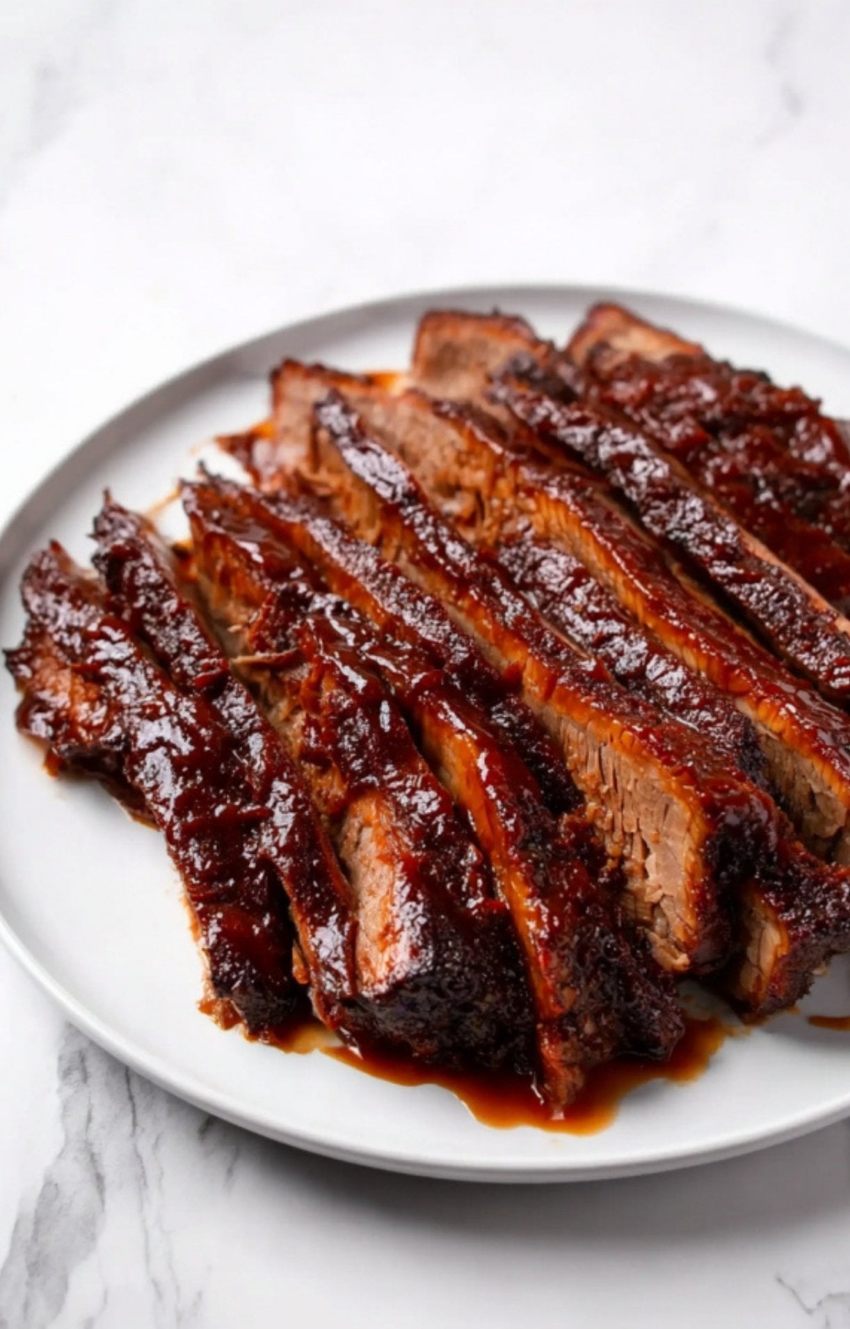 A white plate filled with perfectly uniform slices of oven smoked beef brisket, showcasing a dark bark and rich sauce.