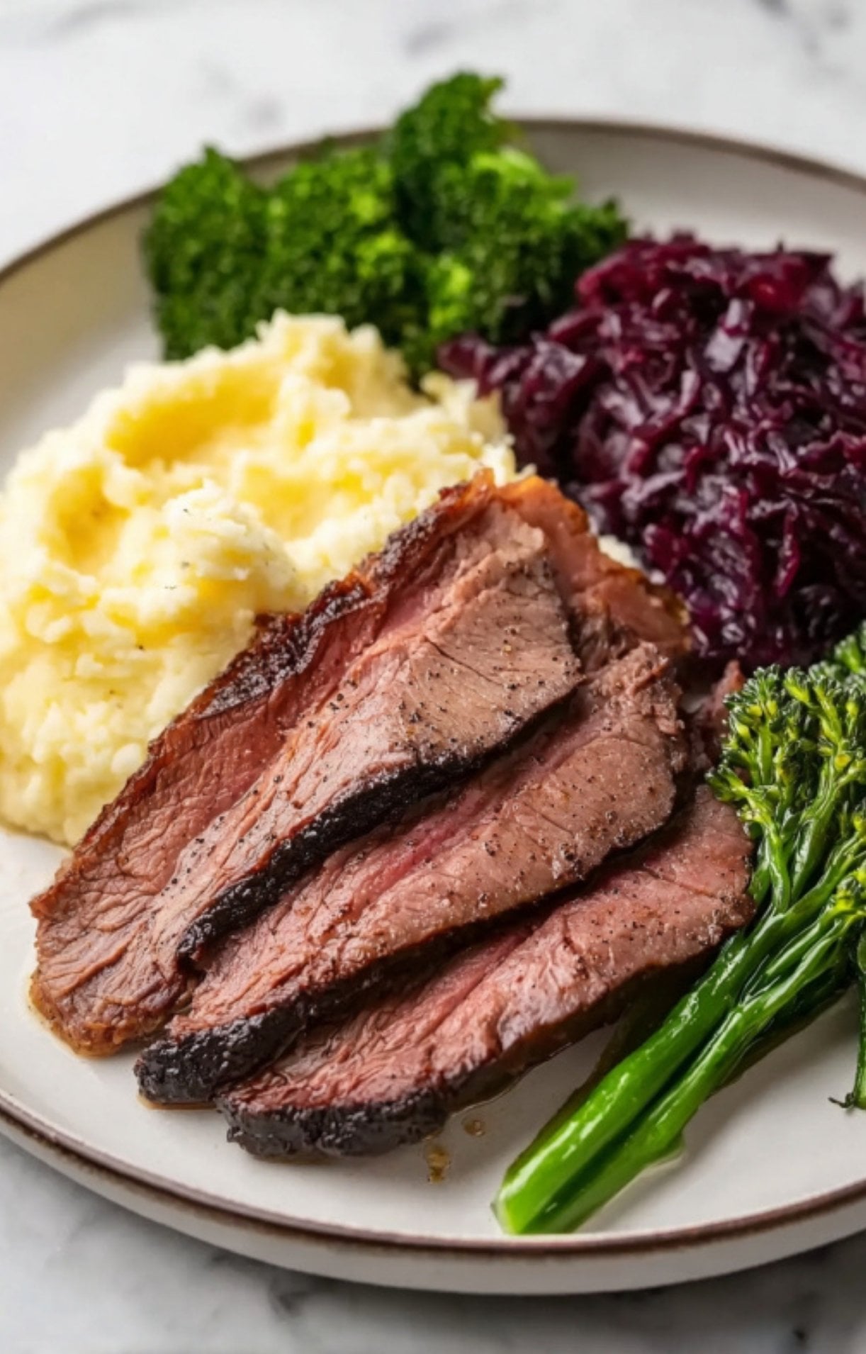 A plated meal featuring tender slices of smoked beef cheeks served with creamy mashed potatoes, steamed broccoli, and braised red cabbage.