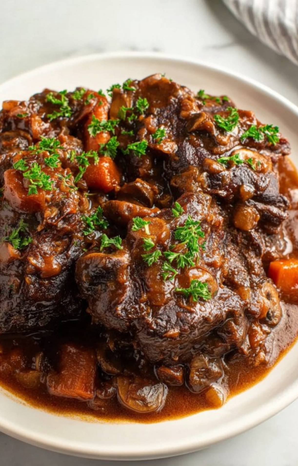 A detailed close-up shot of slow-cooked Beef Cheeks showing the rich texture of the meat and savory sauce with carrots and mushrooms.