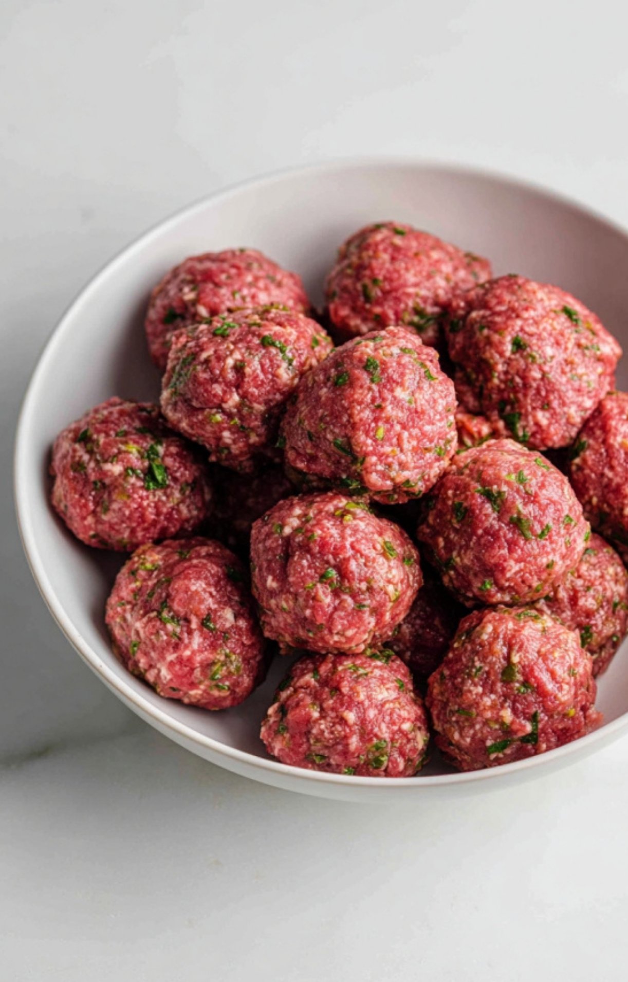 A bowl of hand-rolled raw lamb meatballs featuring visible flecks of herbs and spices.