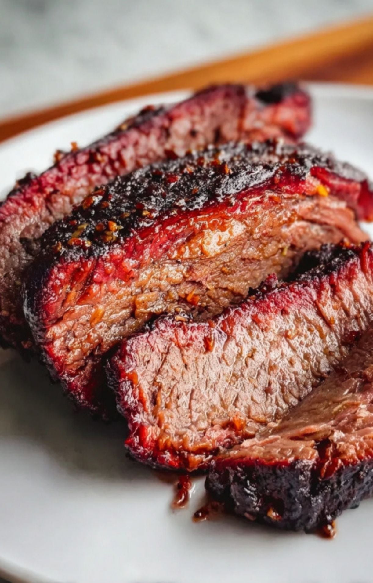 An extreme close-up shot of sliced smoked beef cheeks showing the vibrant red smoke ring, glistening juices, and a dark, peppery bark.