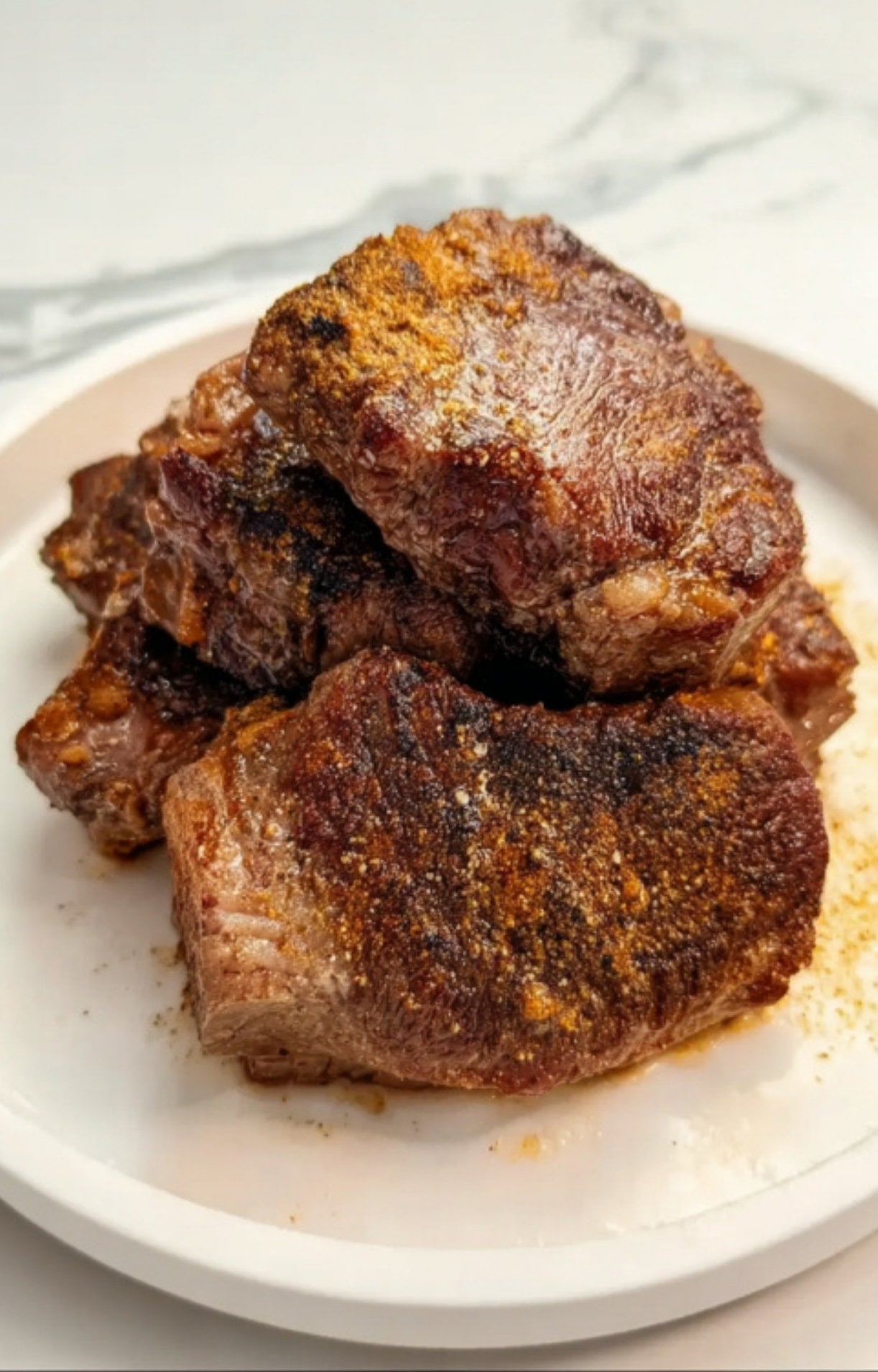A stack of Beef Cheeks on a white plate after being seared to a deep, golden-brown crust.