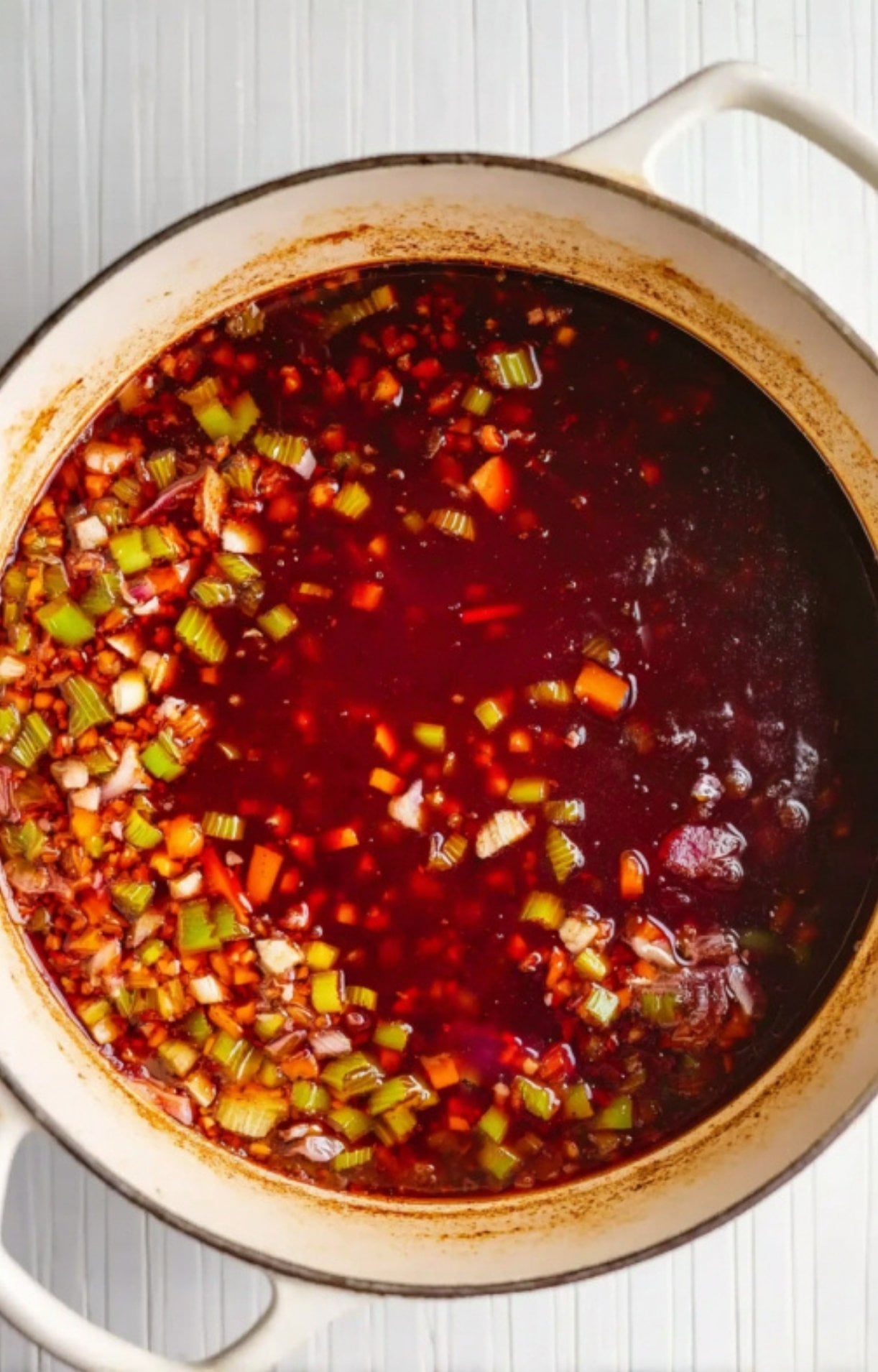 Red wine and beef stock being added to the sautéed vegetables in a Dutch oven to create a rich braising base.