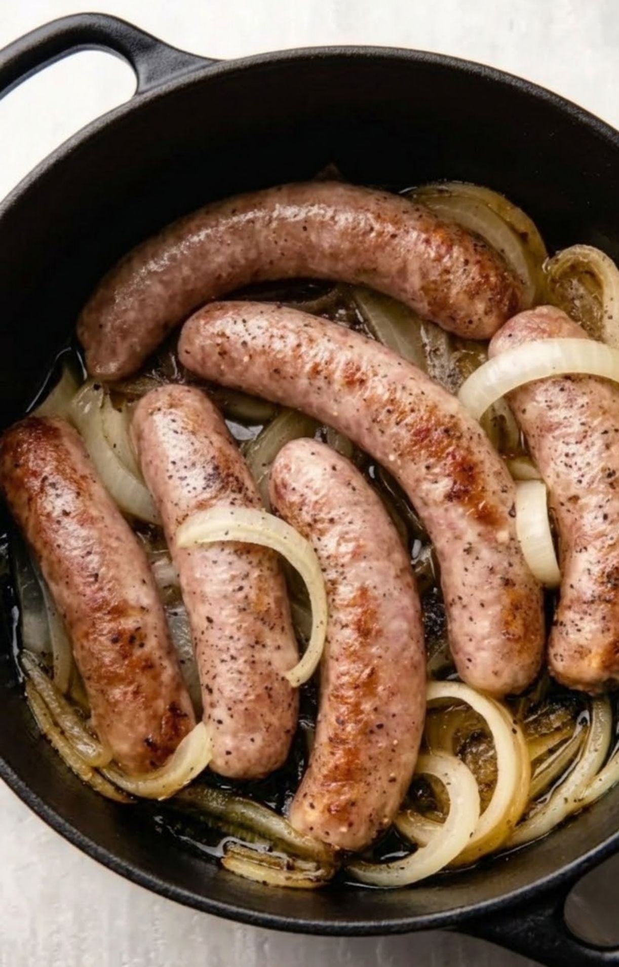 Bratwurst sausages browning in a Dutch oven with softened onions and a light beer broth.