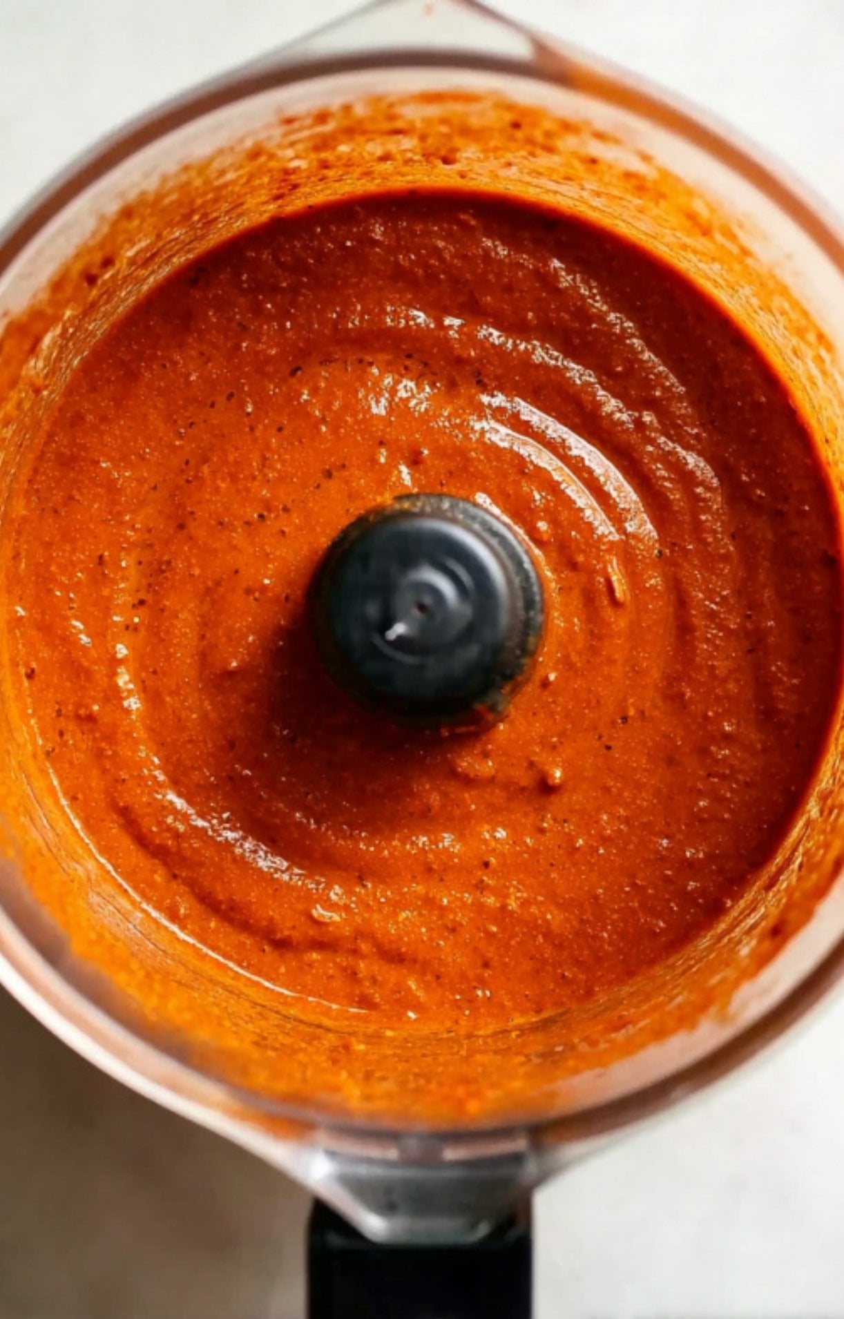 A smooth, vibrant orange-red chile sauce inside a food processor, ready to braise the beef.