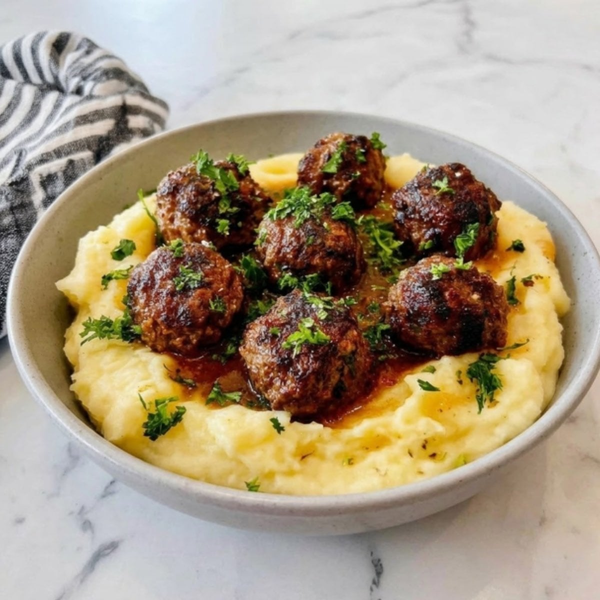A bowl of golden mashed potatoes topped with six browned air fryer beef meatballs and fresh parsley.