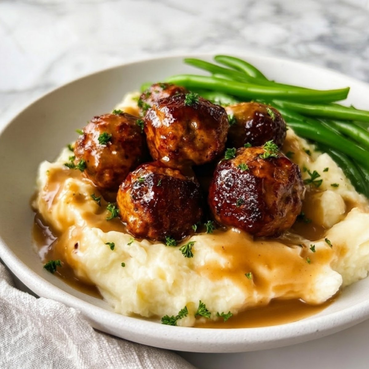 Savory chicken meatballs glazed in gravy served over creamy mashed potatoes with a side of steamed green beans.