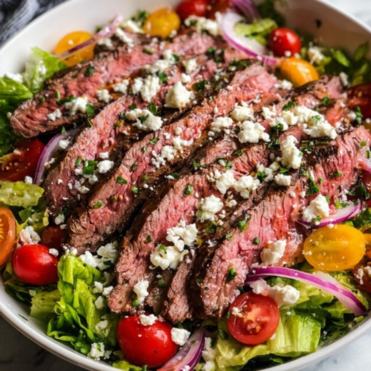 A vibrant bowl of Flank Steak Salad Recipe featuring medium-rare steak slices over greens with tomatoes and feta.