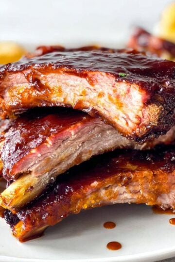 A close-up stack of sliced pork ribs showing a glistening BBQ glaze and tender meat, part of a Pellet Smoker Ribs Recipe.