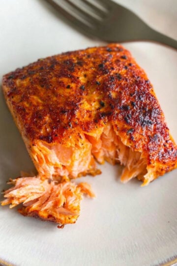 A close-up shot of a cooked sockeye salmon air fryer fillet on a white plate with a fork, showing the moist, flaky interior.