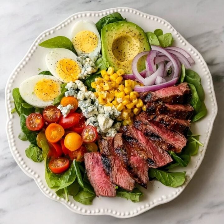 A completed Steak Cobb Salad served on a scalloped white plate, perfectly balanced with protein, healthy fats, and fresh vegetables.