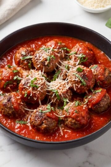 close up wagyu beef meatballs with marinara sauce parmesan cheese and basil garnish