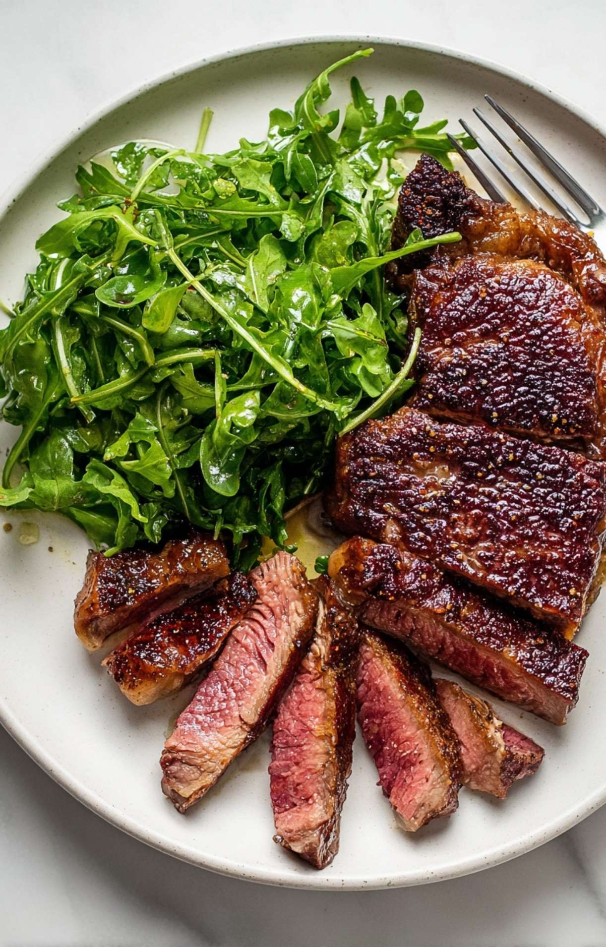 An overhead shot of the completed steak arugula salad on a ceramic plate with a fork, highlighting the contrast between the charred meat and bright greens.